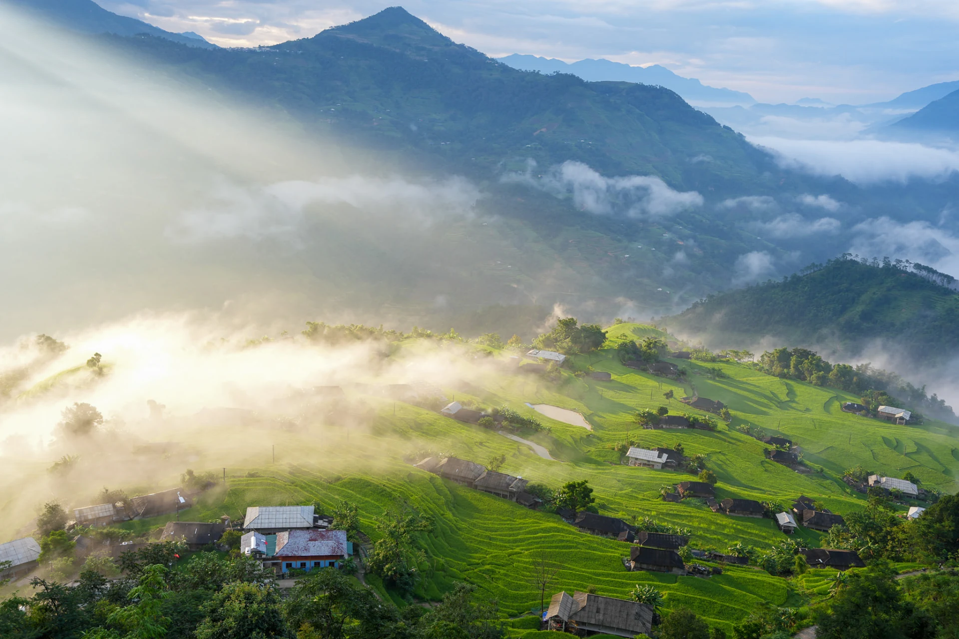 Sunlight over green terraced fields beneath mist-covered mountains